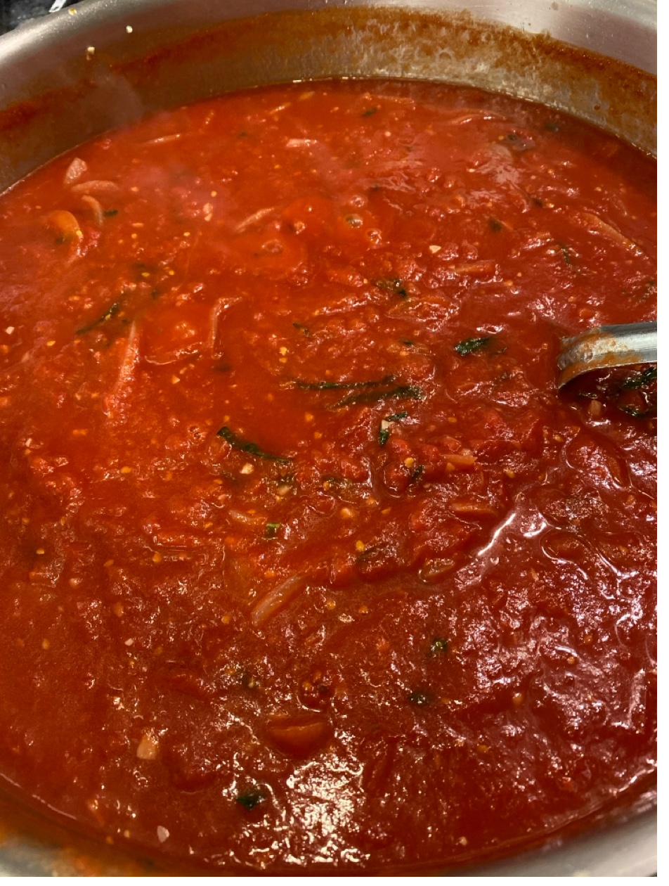 House made tomato sauce simmering in pot with fresh herbs