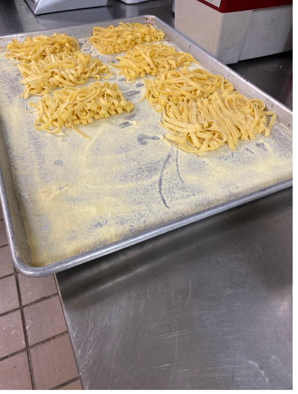 Fresh handmade tagliatelle pasta nests on baking sheet in professional kitchen