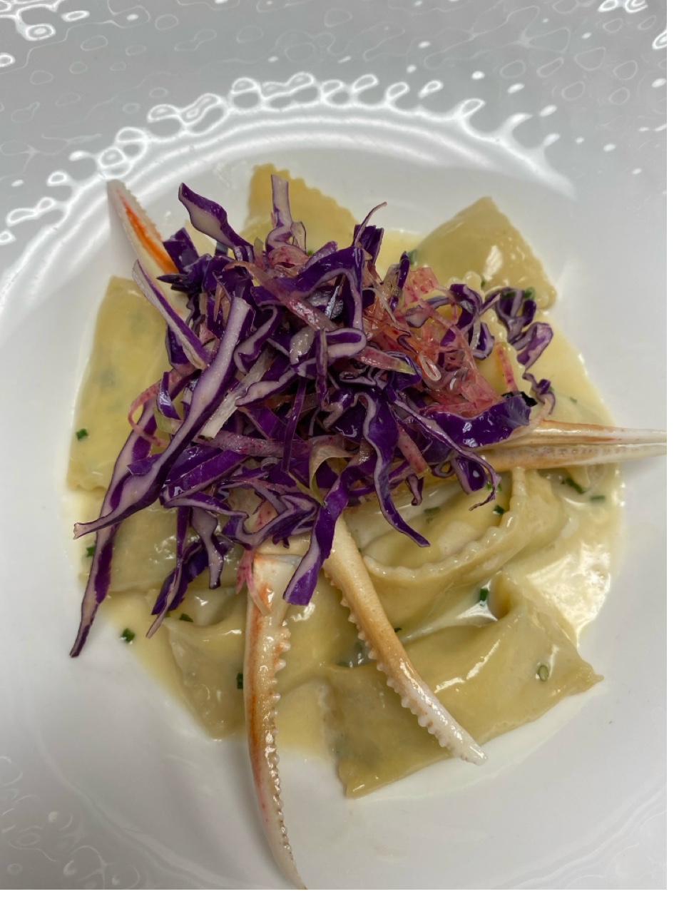 Handmade crab ravioli in cream sauce topped with purple cabbage slaw and crab leg
