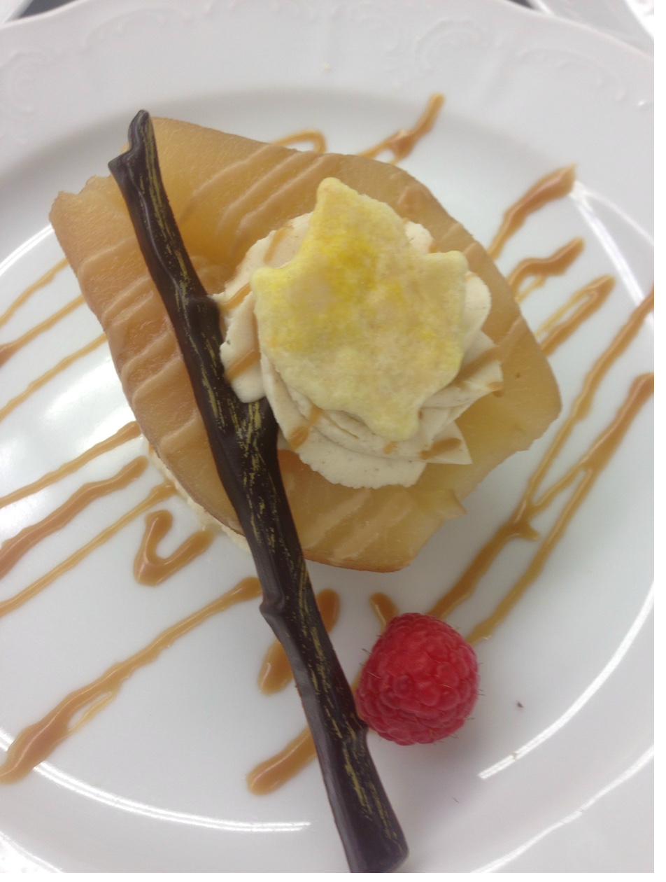 Poached pear dessert with mascarpone cream, chocolate twig, caramel drizzle, and fresh raspberry on white plate