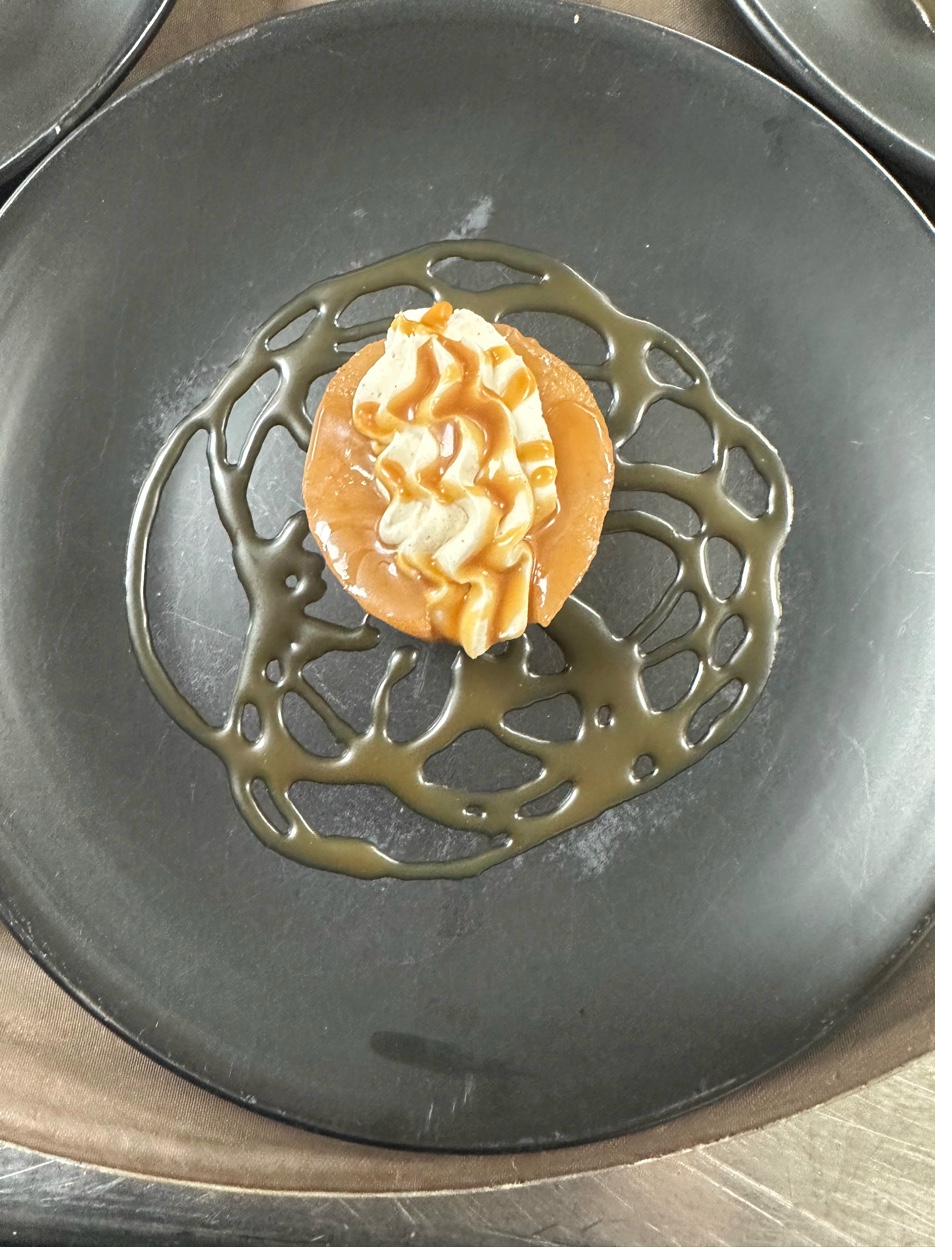 Overhead view of caramelized poached pear with whipped cream on black plate with decorative caramel web