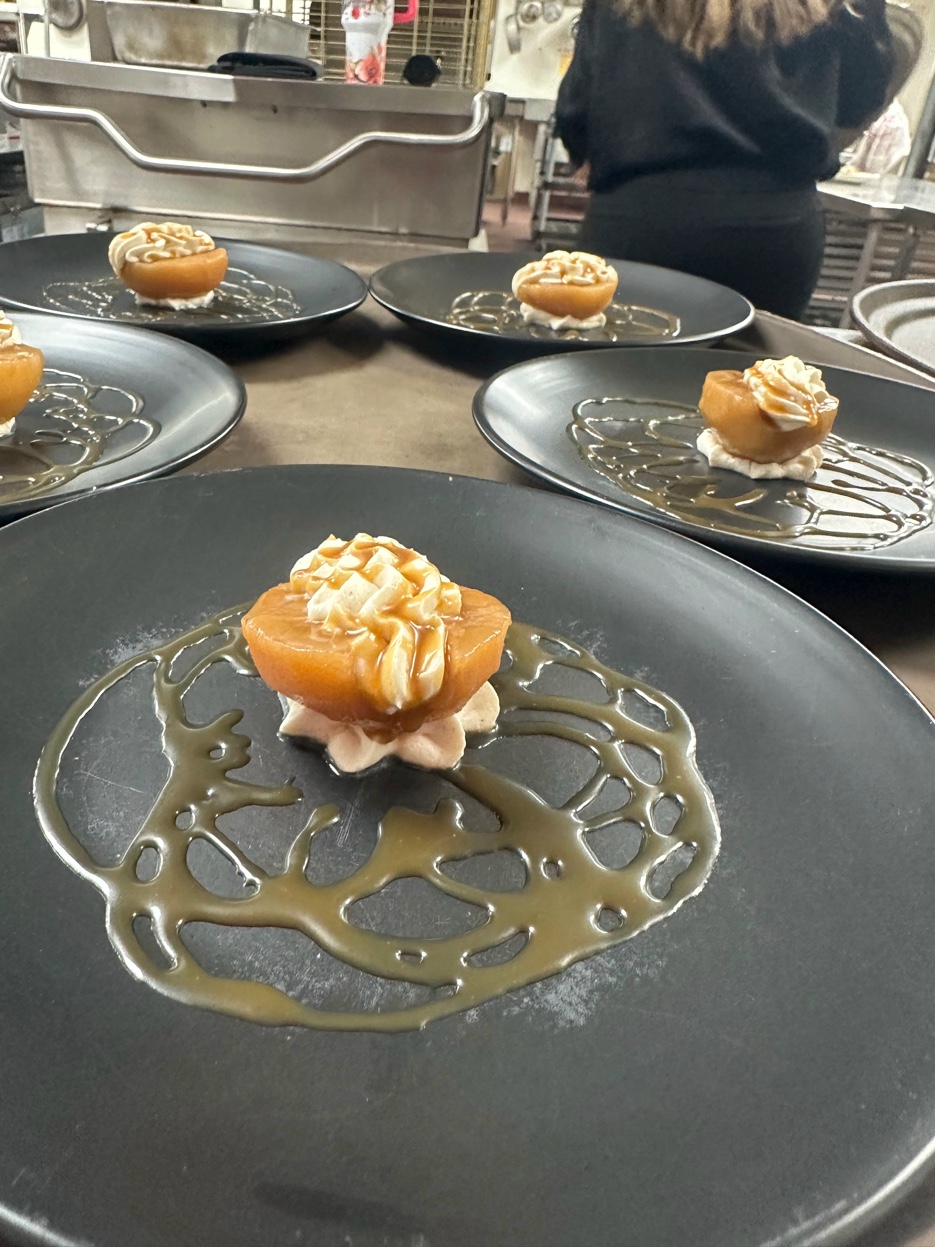 Multiple black plates with caramelized pear desserts being plated in professional kitchen