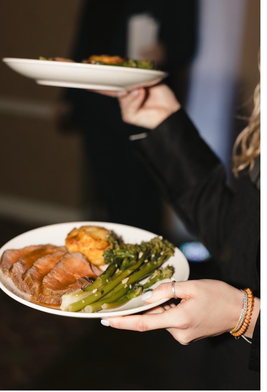 Server carrying plated prime rib with broccolini and roasted potato at private dinner event