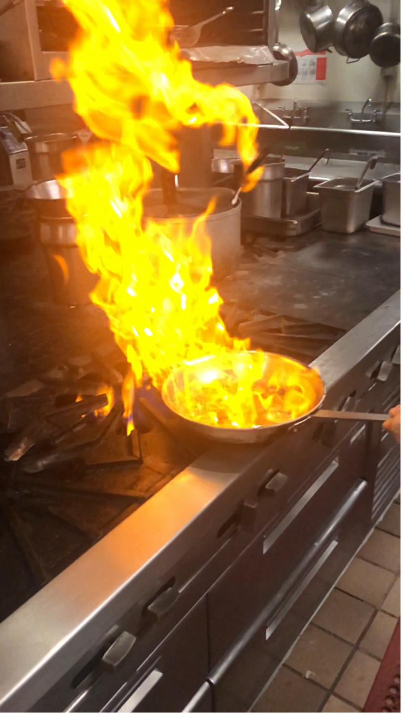 Dramatic flambé technique with flames rising from sauté pan in professional kitchen