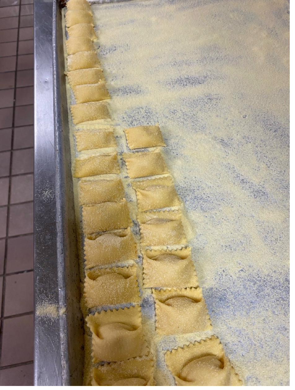 Rows of fresh handmade ravioli dusted with semolina on commercial baking sheet