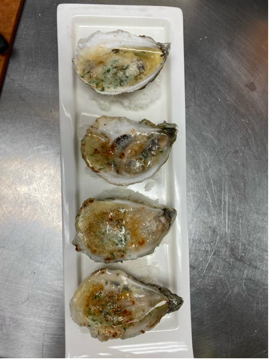 Four baked oysters with herb butter on white plate with coarse salt bed