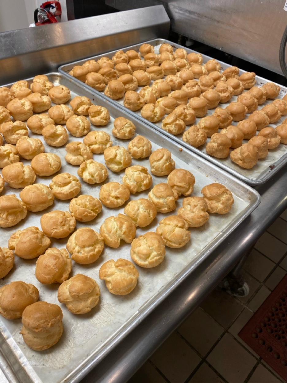 Trays of freshly baked profiterole cream puffs cooling in professional kitchen