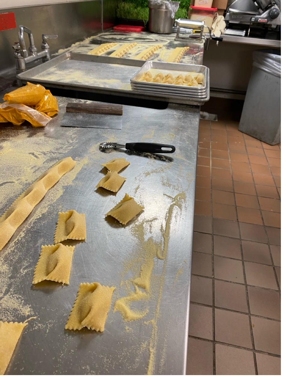 Fresh ravioli being made by hand on stainless steel counter with pasta wheel and semolina