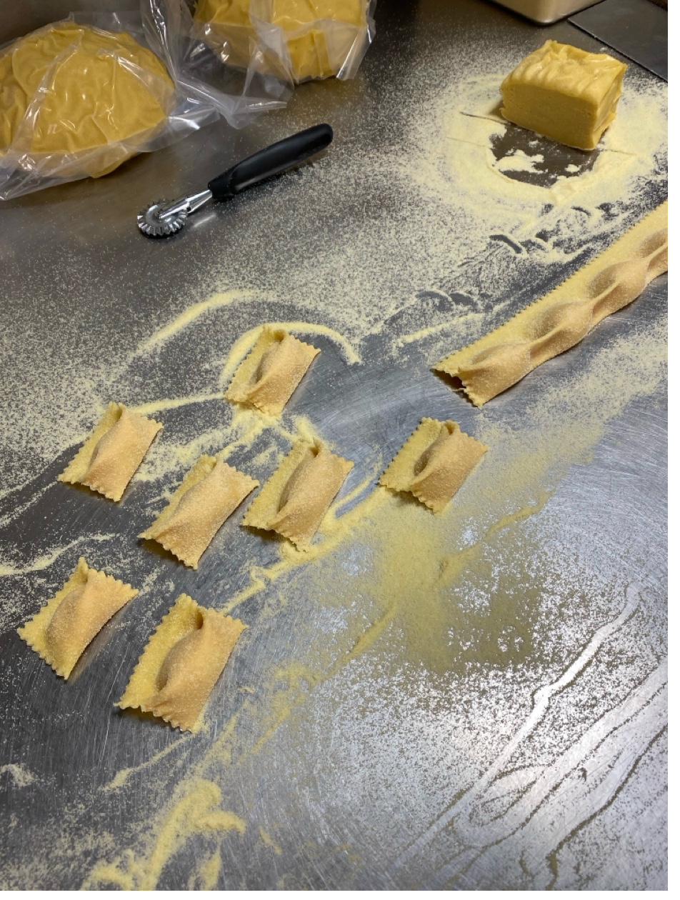 Freshly cut ravioli pieces on floured stainless steel counter with pasta wheel