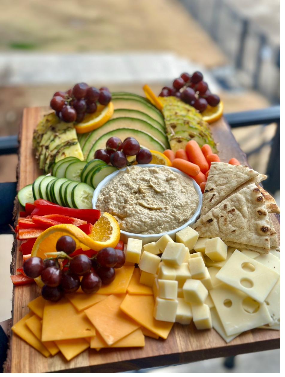 Artisan cheese board with assorted cheeses, hummus, pita, fresh fruit and vegetables on natural wood slice