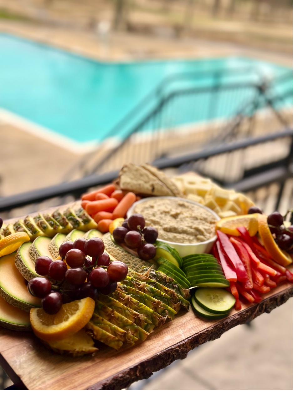 Fresh fruit and vegetable grazing board with hummus on wood slice by the pool