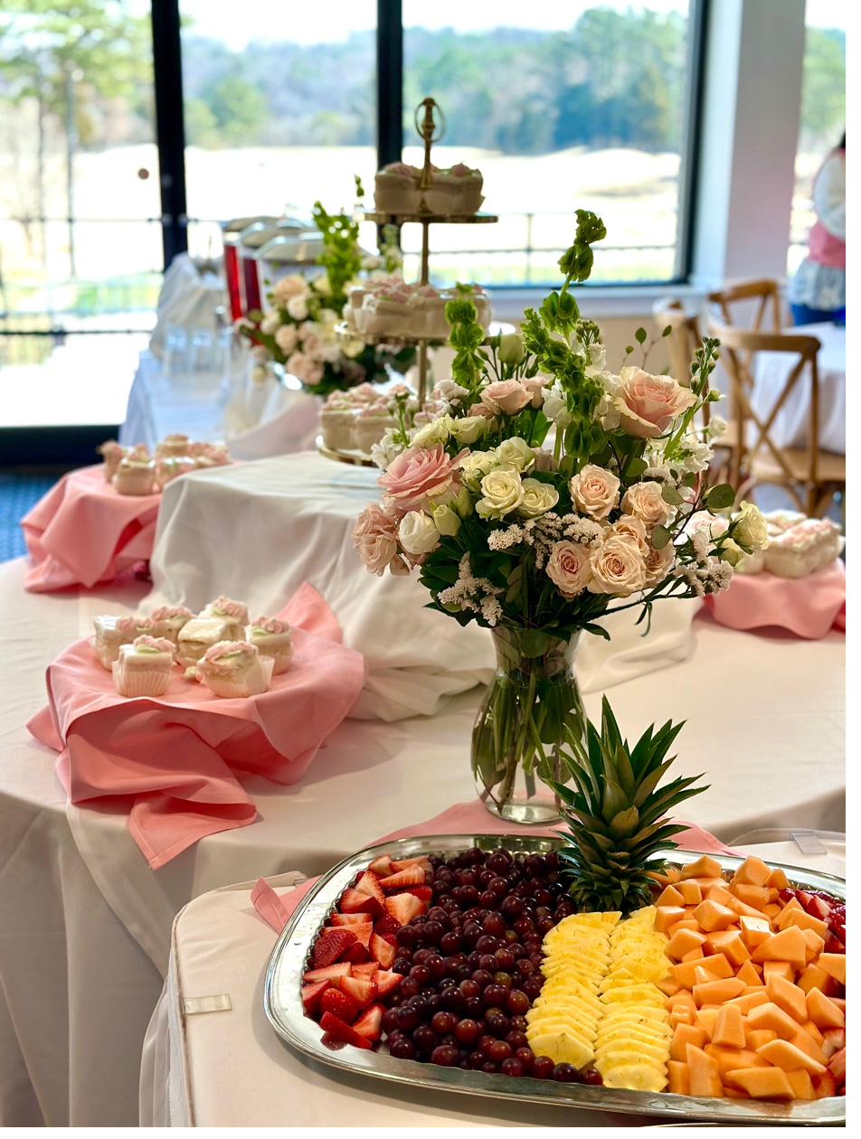 Elegant event table setup with fresh fruit platter, pink roses, cupcakes, and tiered cake stand